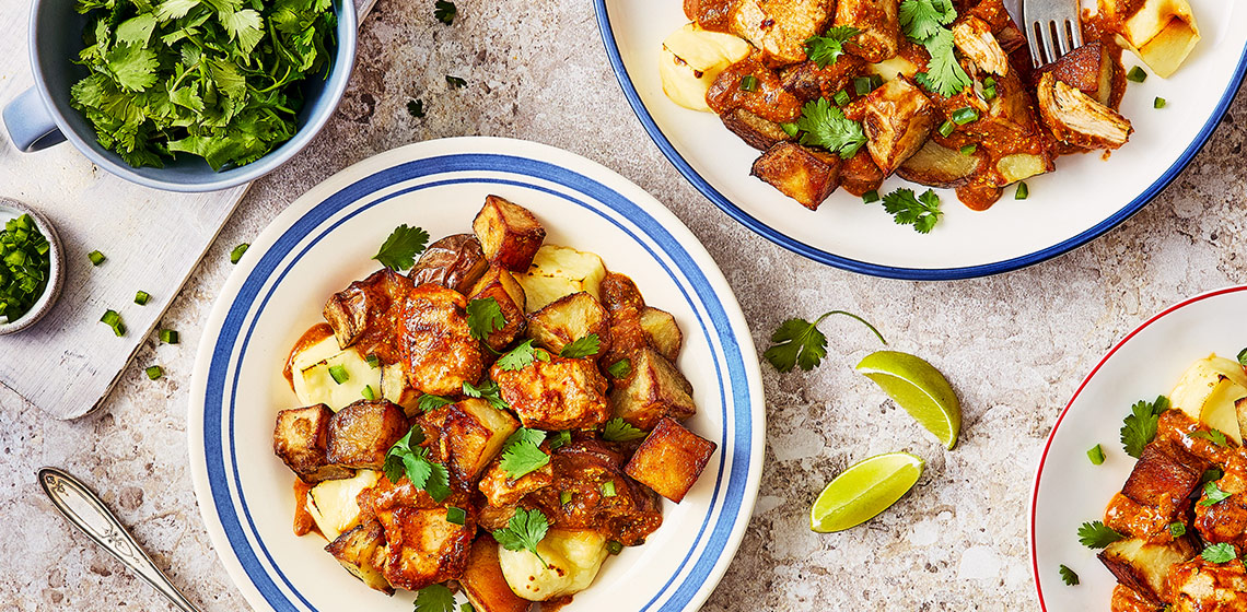 Three bowls of Butter Chicken Poutine with limes, cutlery, and herbs around the bowls on the table.
