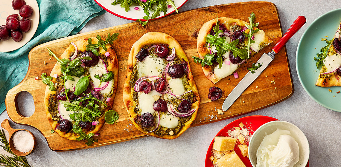 Two full cherry and basil flatbreads on a cutting board, and one that has been cut in half.
