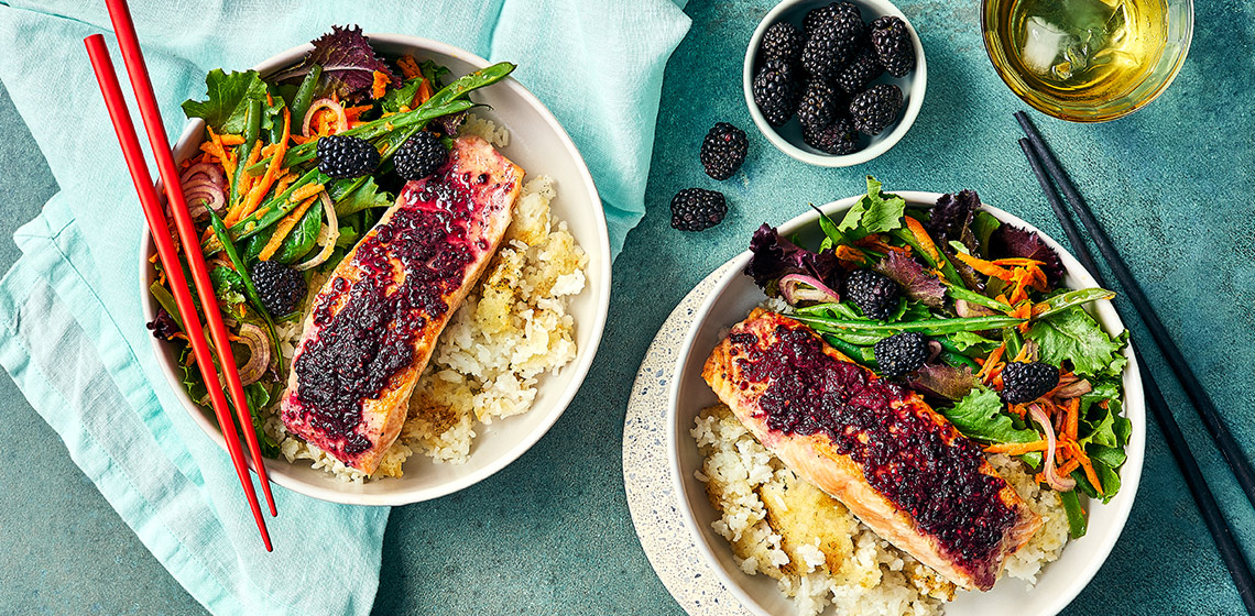 Two crispy rice bowls topped with vegetables, salmon filet and a blackberry glaze.