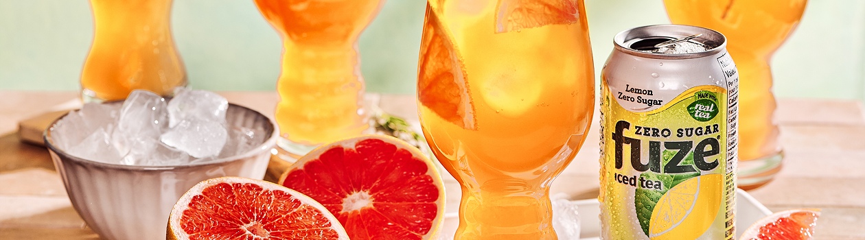 Lemon iced tea is served in a tall glass with ice and rosemary with two half sliced grapefruit on the left side.