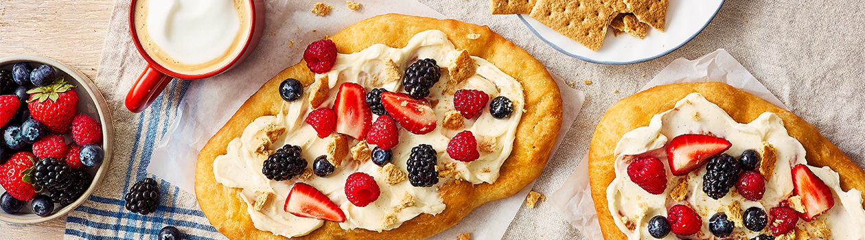 Two sweet fried pastries topped with cream cheese icing, fresh berries, and graham crumbs.